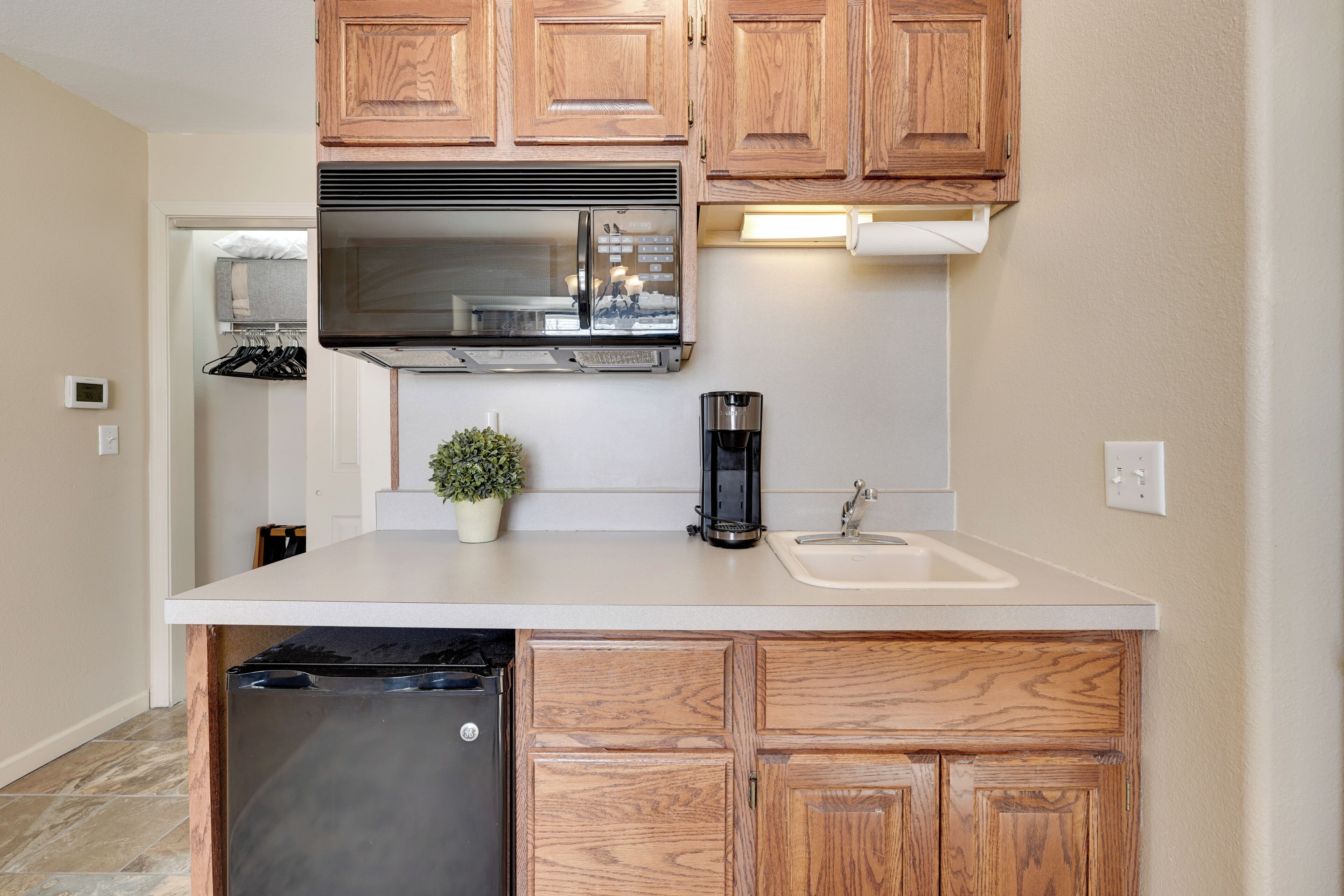 A compact kitchen with wooden cabinets, a stainless steel refrigerator, a built-in microwave, a coffee maker, and a sink.