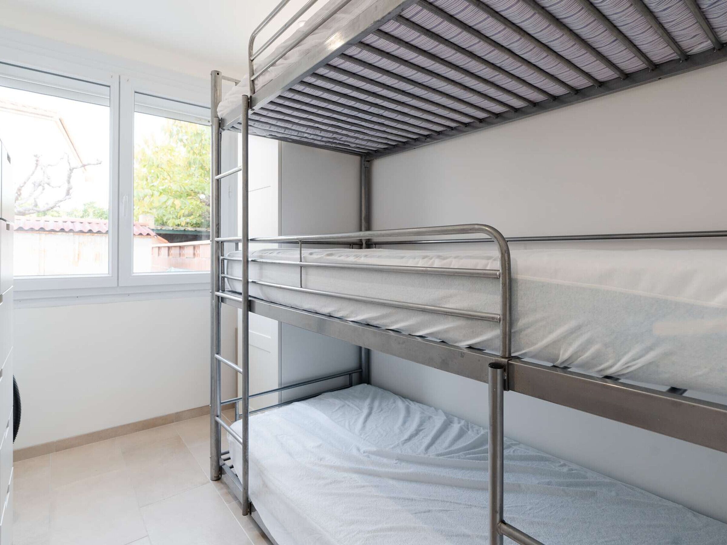 Une chambre avec des lits superposés dotés de barrières métalliques, une fenêtre et une vue sur l’extérieur.