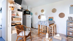 A cozy kitchen with a dining area, wicker furniture, and a TV mounted on the wall. - 1-bedroom apartment with balcony, private parking, pets allowed (Fleury-Saint-Pierre-la-Mer)