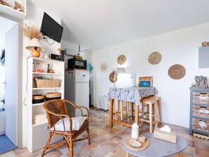 A cozy kitchen with a dining area, wicker furniture, and a TV mounted on the wall. - 1-bedroom apartment with balcony, private parking, pets allowed (Fleury-Saint-Pierre-la-Mer)