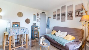 A cozy living room with a sofa, a small table, and a coffee table. There are wall decorations and a door leading to another room. - 1-bedroom apartment with balcony, private parking, pets allowed (Fleury-Saint-Pierre-la-Mer)