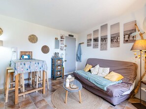 A cozy living room with a sofa, a small table, and a coffee table. There are wall decorations and a door leading to another room. - 1-bedroom apartment with balcony, private parking, pets allowed (Fleury-Saint-Pierre-la-Mer)