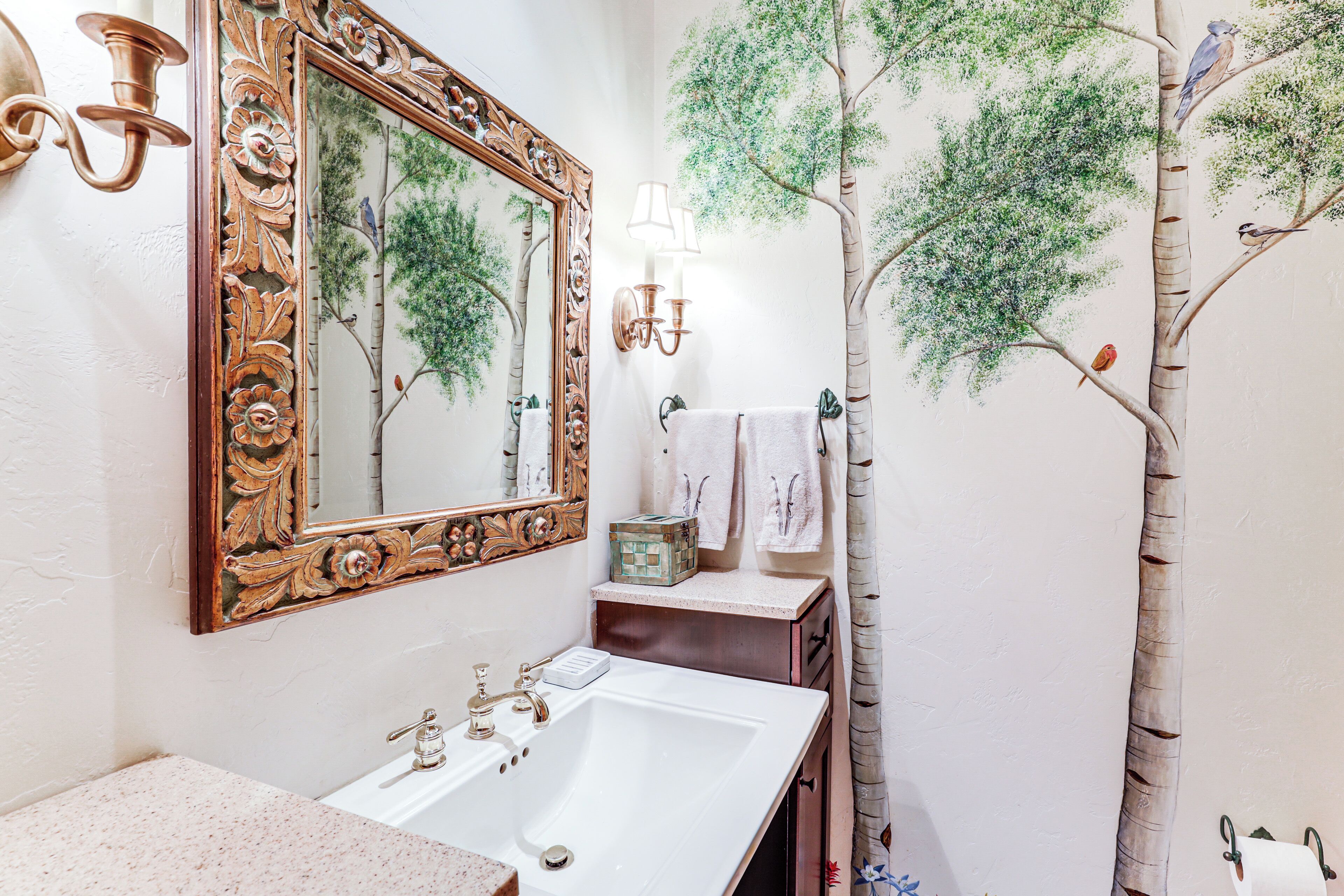 A bathroom with a large mirror, a sink, and a wall mural of trees.