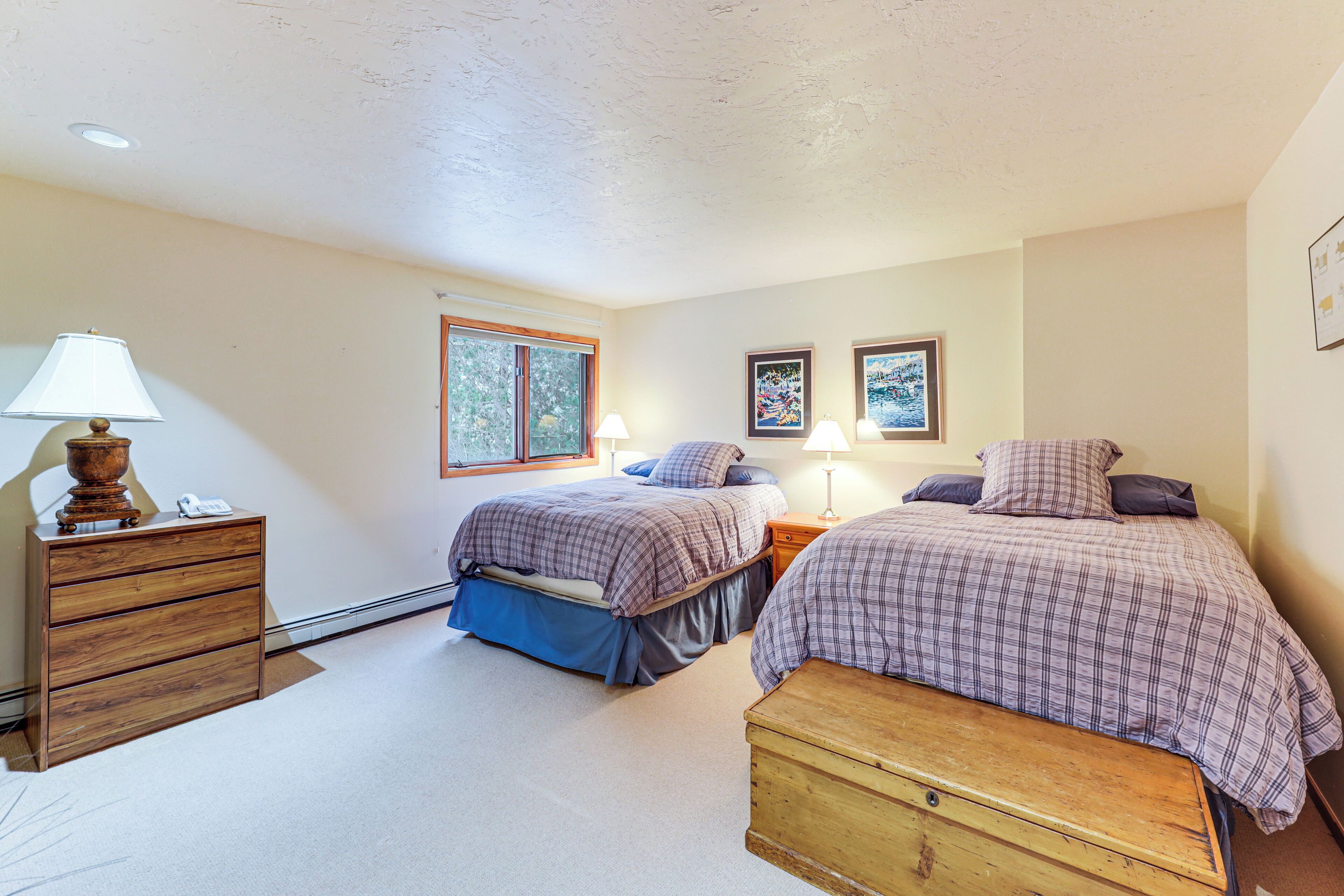 A bedroom with two beds, a dresser, a bench, and a window.