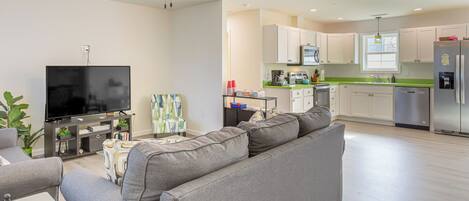 A modern living room with a grey sofa, a flat-screen TV, and a ceiling fan.