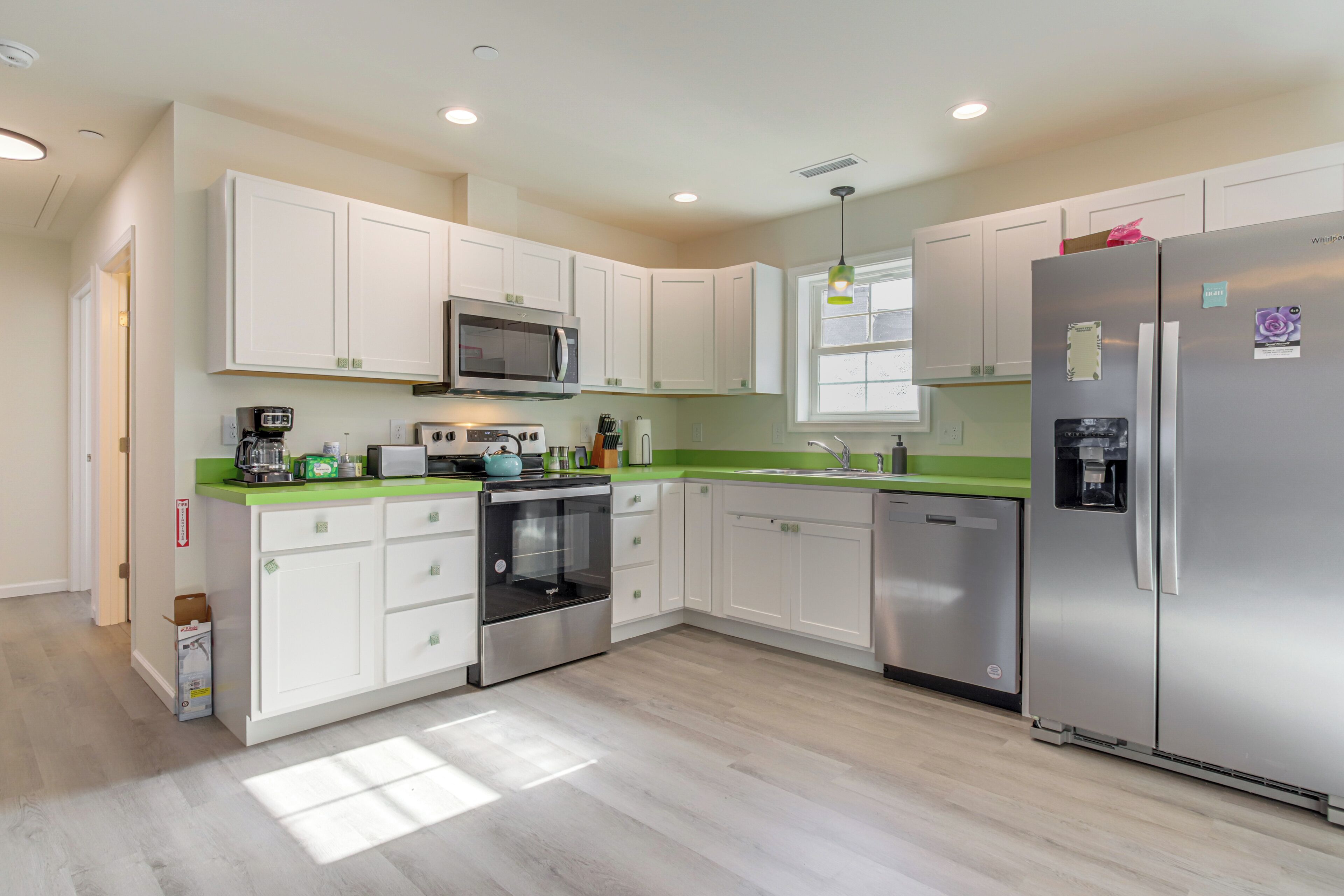A modern kitchen with white cabinets, stainless steel appliances, and a green countertop.