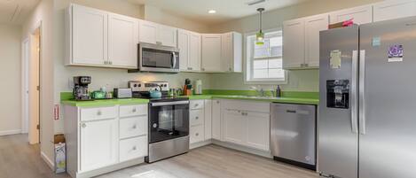 A modern kitchen with white cabinets, stainless steel appliances, and a green countertop.