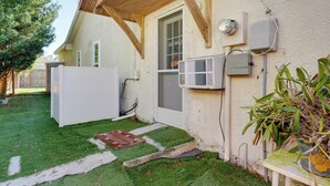Una casa con facciata bianca, un portico in legno, una porta e un piccolo giardino con erba sintetica e un ciottolo.
