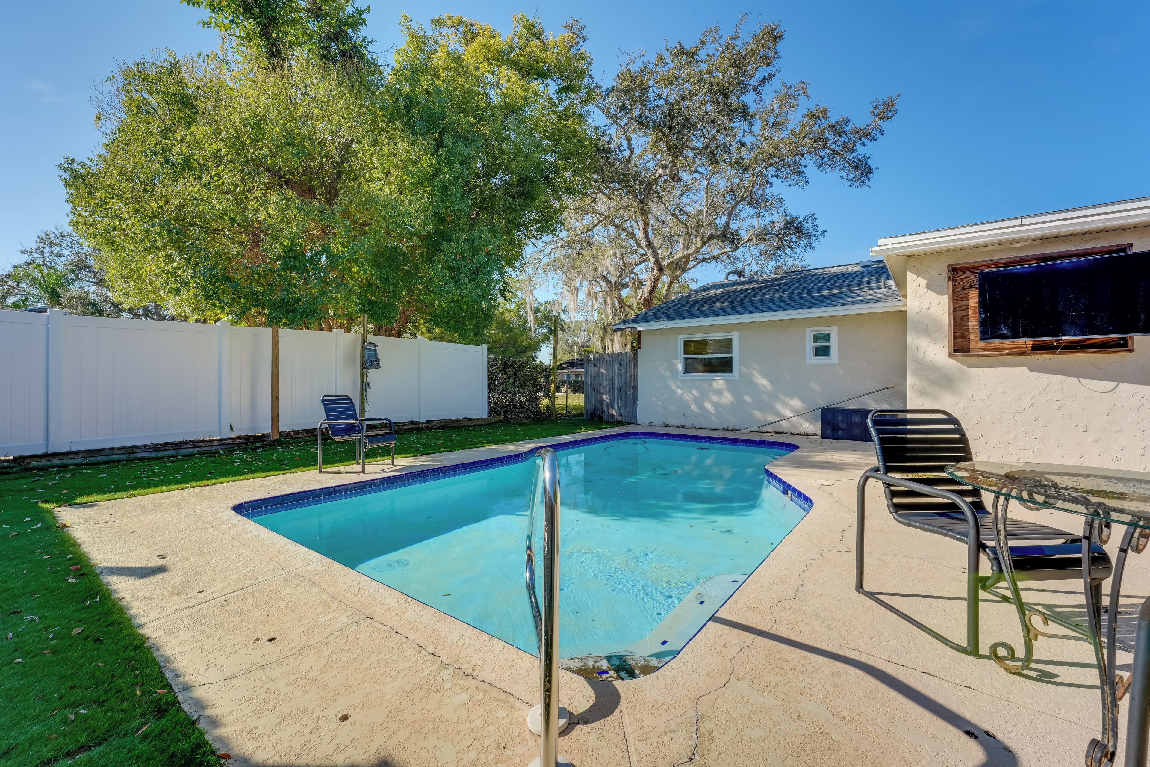 A backyard with a swimming pool, a covered patio area, and a small house.