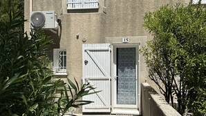 Um edifício com fachada bege, uma porta branca com placa de identificação '15' e um aparelho de ar condicionado fixado na parede.