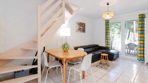 Uma sala de estar moderna com escada de madeira, um sofá de couro preto, uma mesa de jantar de madeira com cadeiras brancas e um tapete colorido.