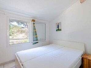 Une petite pièce propre, avec un lit simple, une fenêtre avec un rideau et un petit tableau accroché au mur.