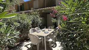 Um pátio externo com uma mesa posta para dois, rodeado por vegetação exuberante e plantas floridas.