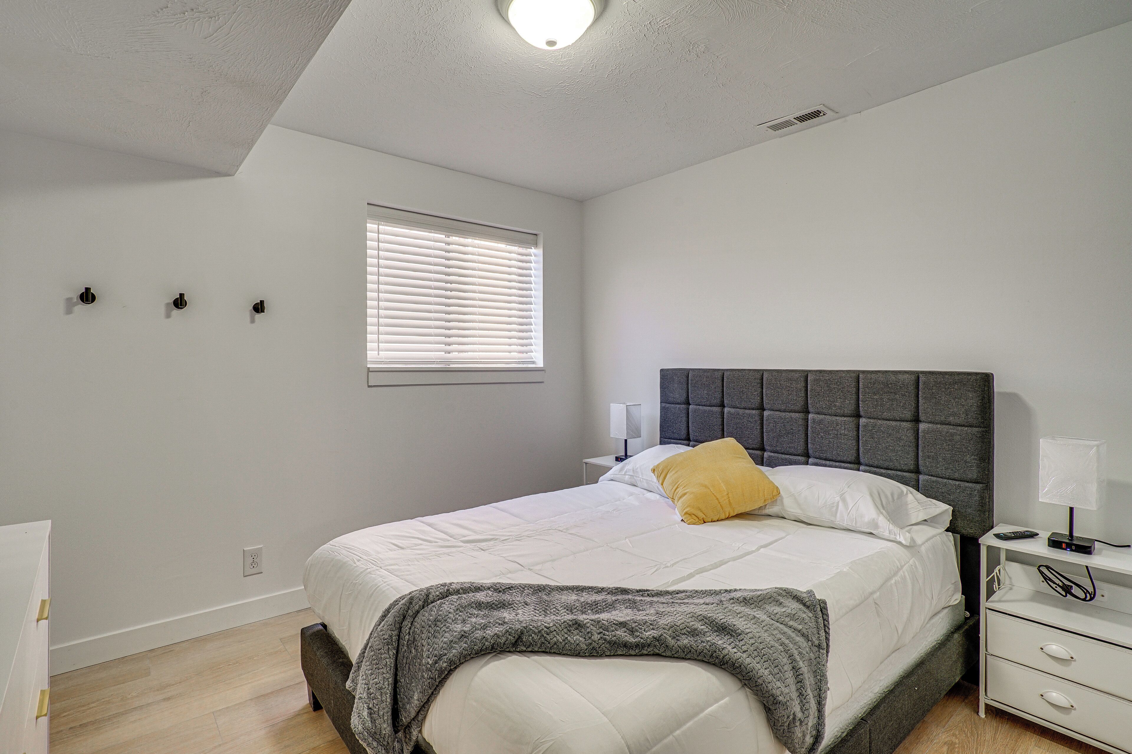 A bedroom with a bed, bedside table, lamp, and a window with blinds.