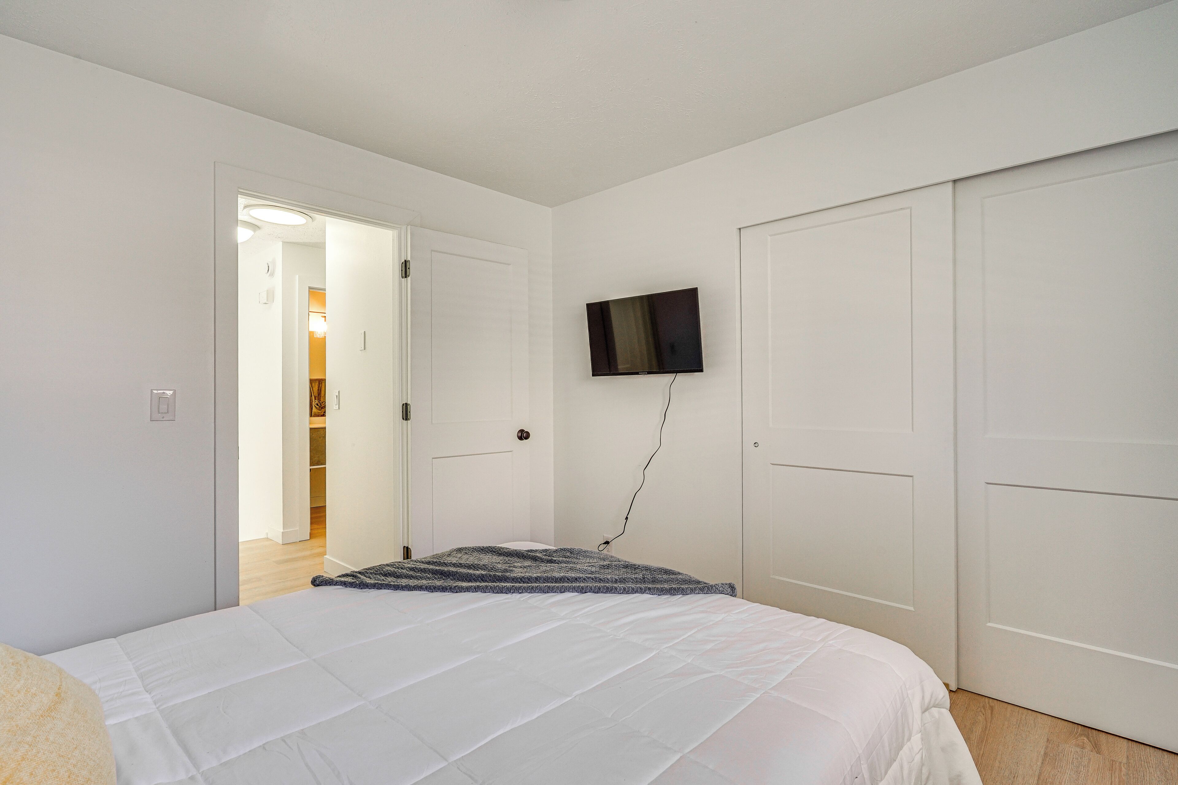 Een slaapkamer met een bed, een aan de muur bevestigde televisie en een deur naar een andere kamer.