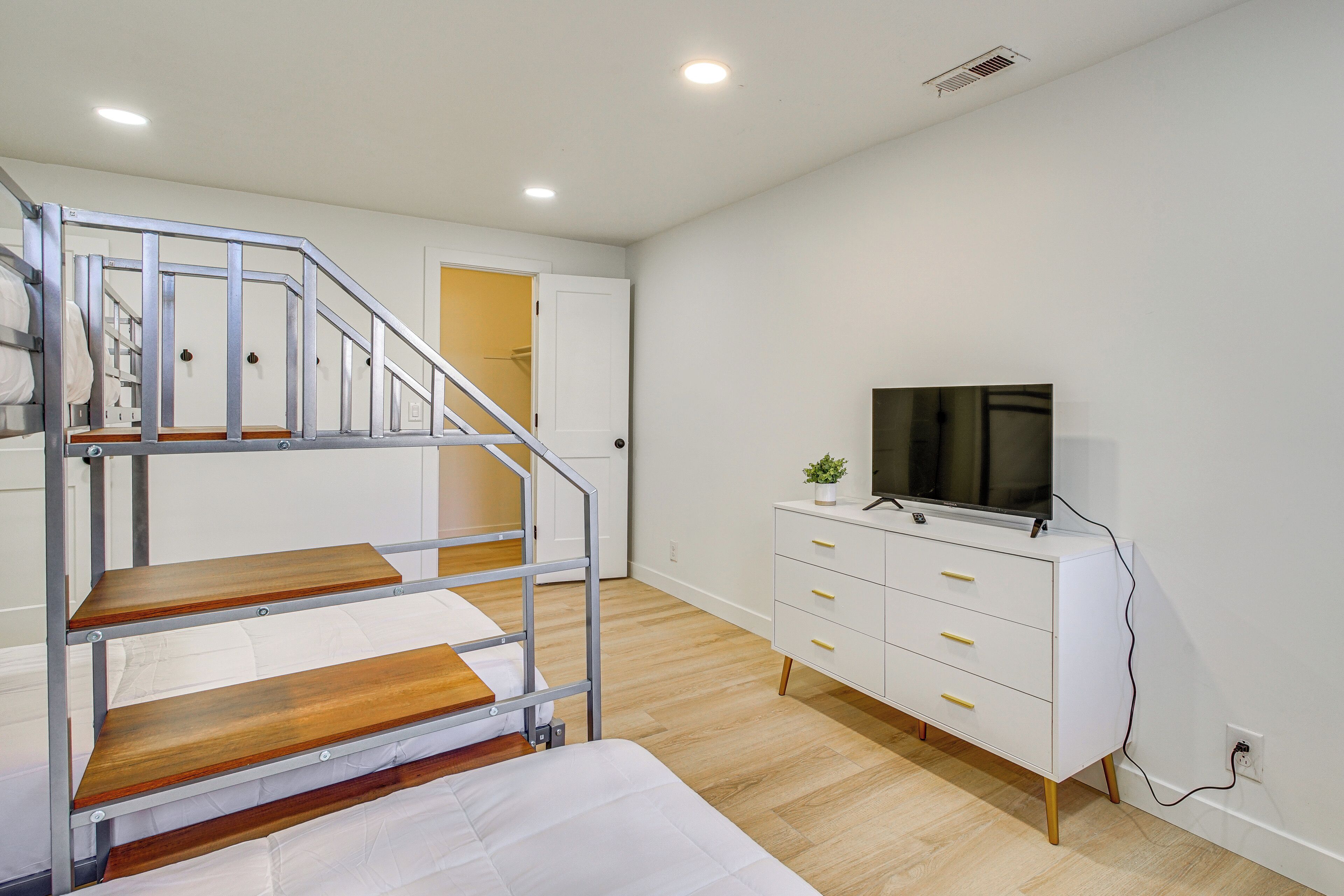 A room with bunk beds, a white dresser, a television, and a door leading to another room.
