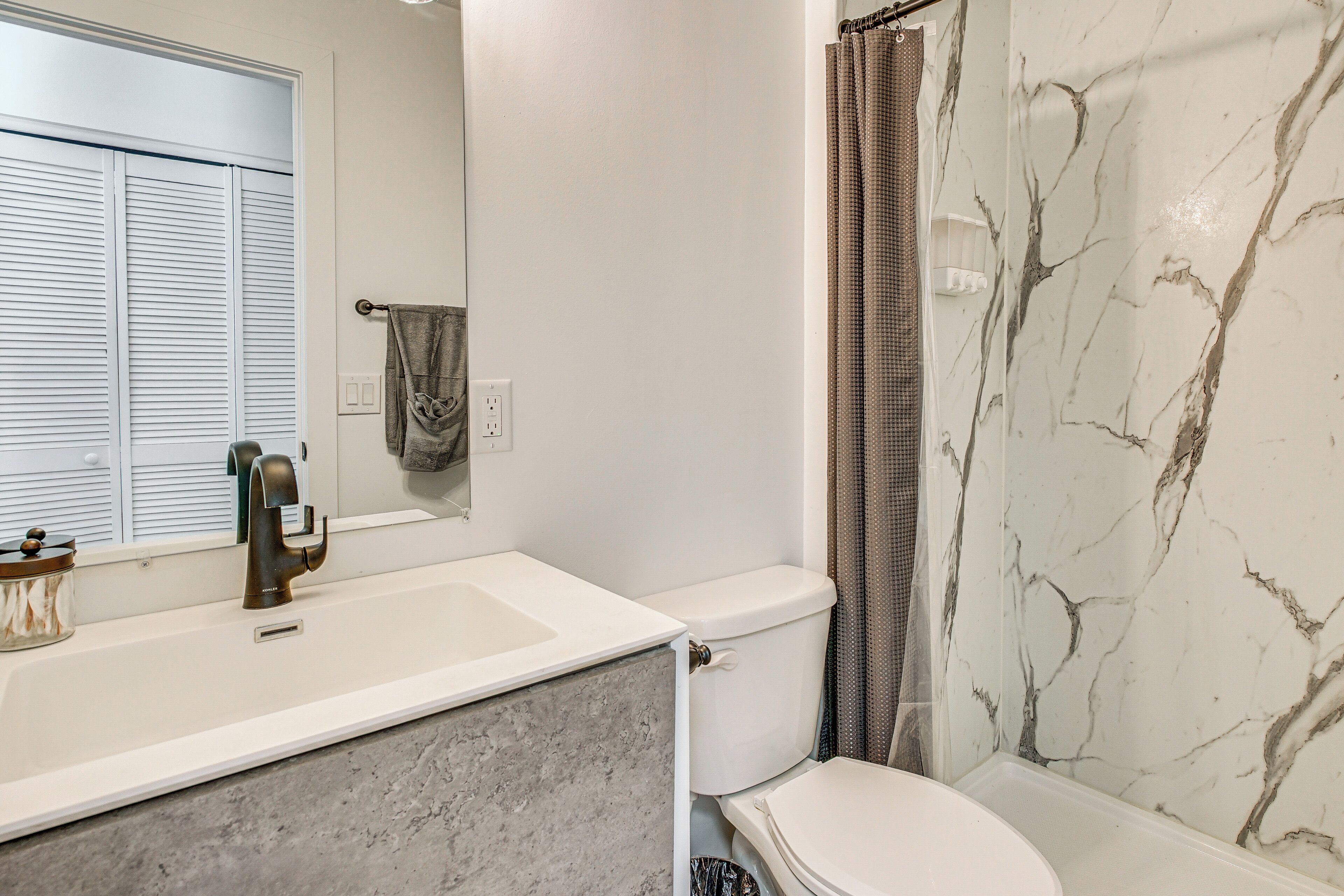 A bathroom with a white sink, a marble shower wall, and a toilet.