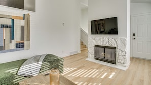 Una sala de estar moderna con chimenea, televisor montado y una escalera que sube a otro nivel.