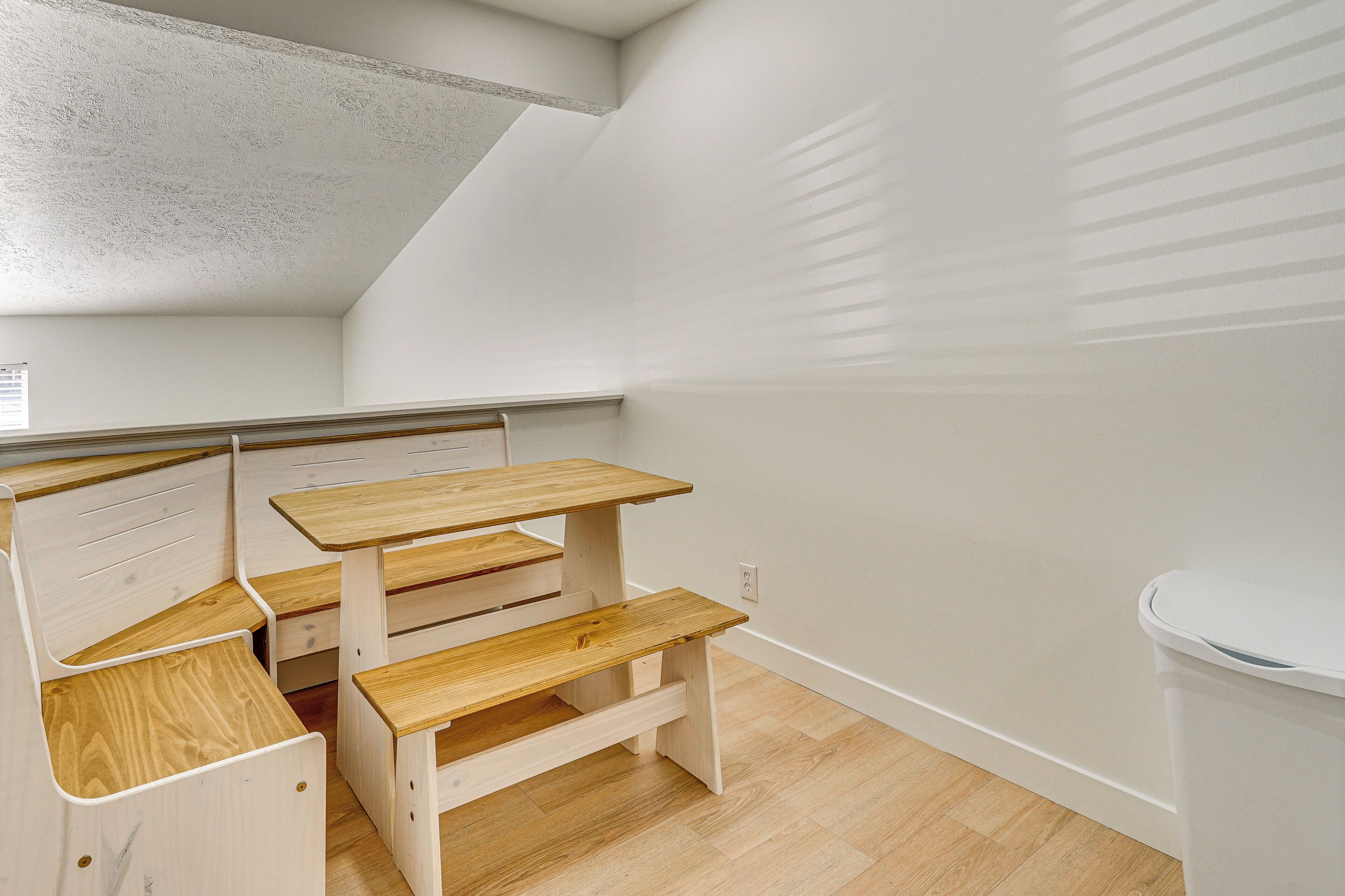 A small, compact room with a wooden desk and bench, white walls, and a sloped ceiling.