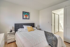 Ein Schlafzimmer mit Bett, Nachttischen, einem Wandbild und einer Tür zu einem anderen Raum.
