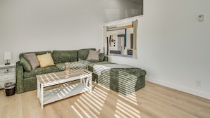 Una sala de estar con un sofá verde, una mesa de centro blanca y un reposapiés estampado.