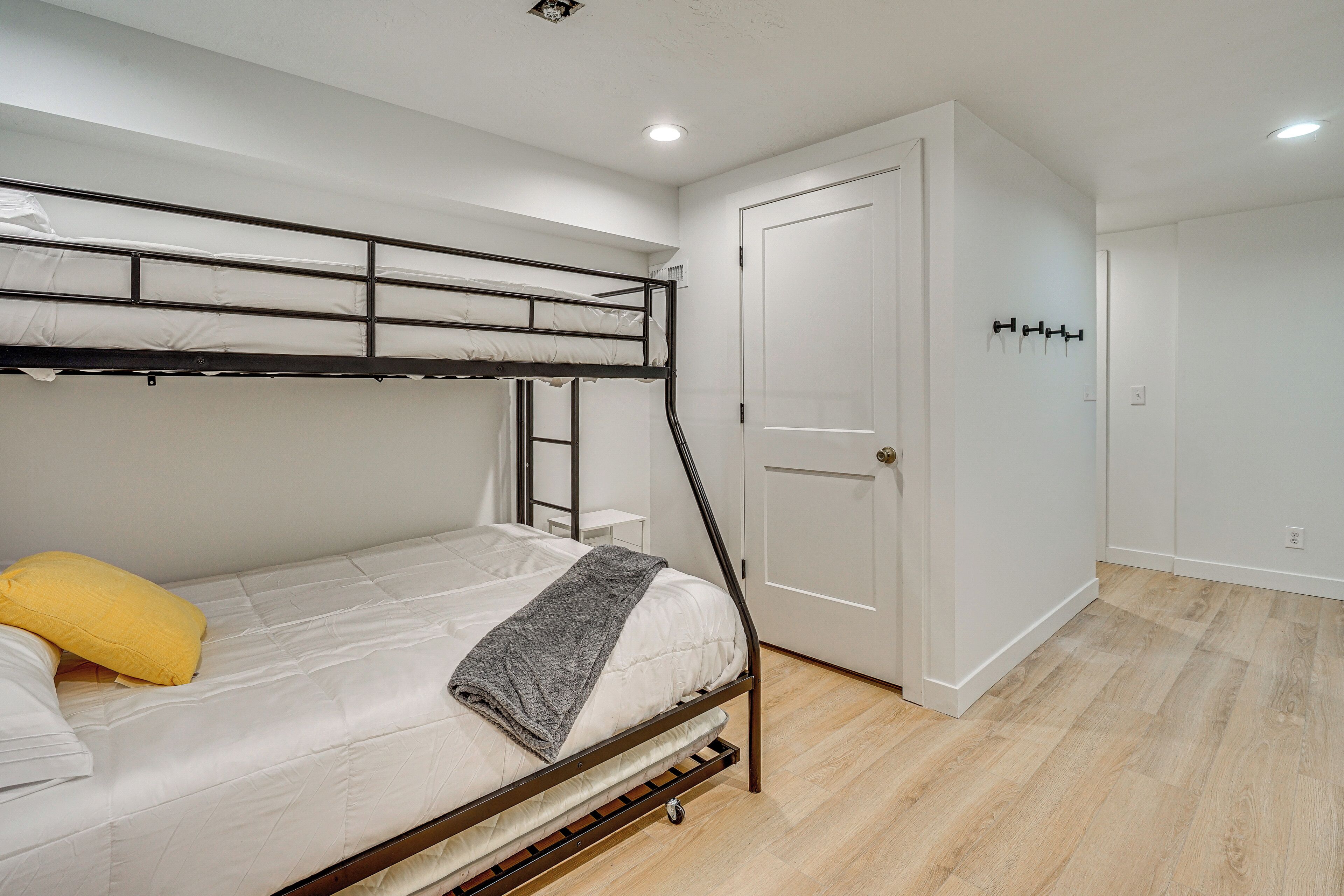Un letto a castello con materasso, cuscini e coperta. Si vede una porta con maniglia e un gancio per cappotti a parete.