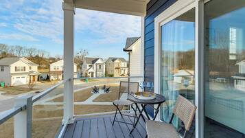 A balcony with a view of neighboring houses, a table with chairs, and a glass door.