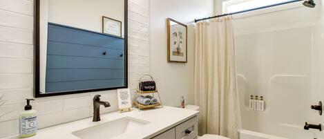 A bathroom with a white sink, a mirror, a toilet, and a bathtub.
