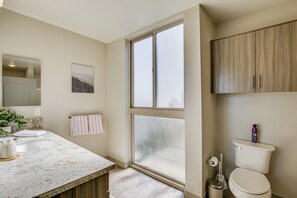 Een badkamer met een groot raam, een wastafel, een toilet en een kast.
