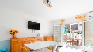 Eine moderne Küche mit Essbereich, einem an der Wand befestigten Fernseher und Blick ins Freie durch eine Schiebetür.