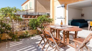 Eine Terrasse mit Holztisch und -stühlen, einer blauen Couch und einer weißen Tür, die zu einem Innenraum führt.