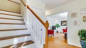 A staircase with wooden steps and a wooden handrail, leading to a room with a television, a red chair, and a potted plant. - Walk to Dtwn & Campus! Spacious Hampton Home (Hampton)