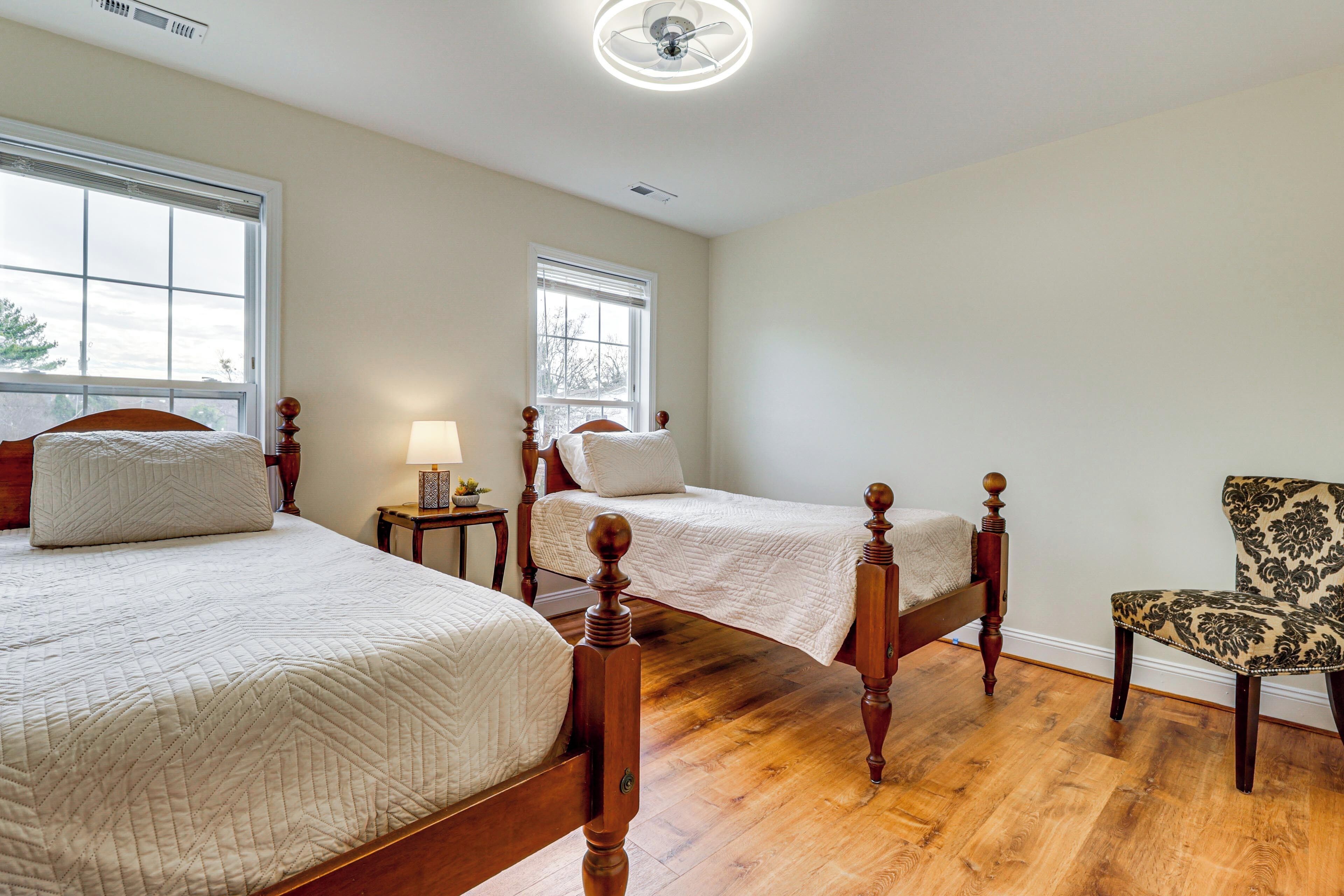 A bedroom with two beds, wooden flooring, a chair, and a ceiling fan.