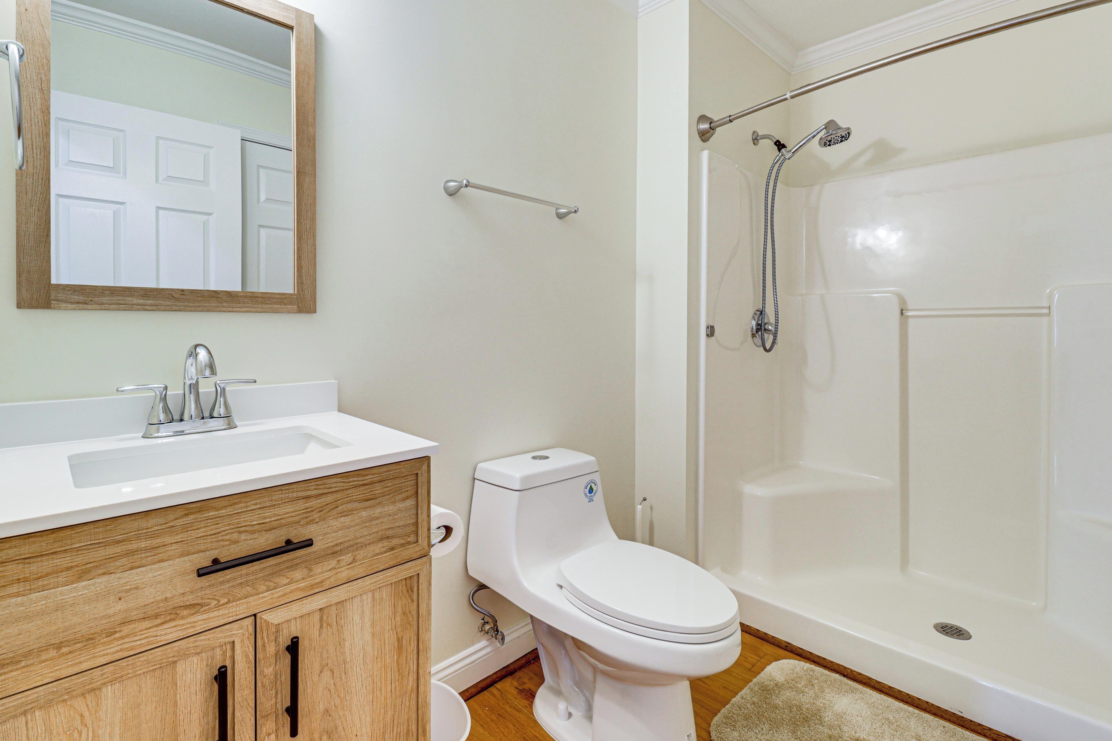 Un baño con lavabo blanco, tocador de madera, inodoro y ducha a ras de suelo.