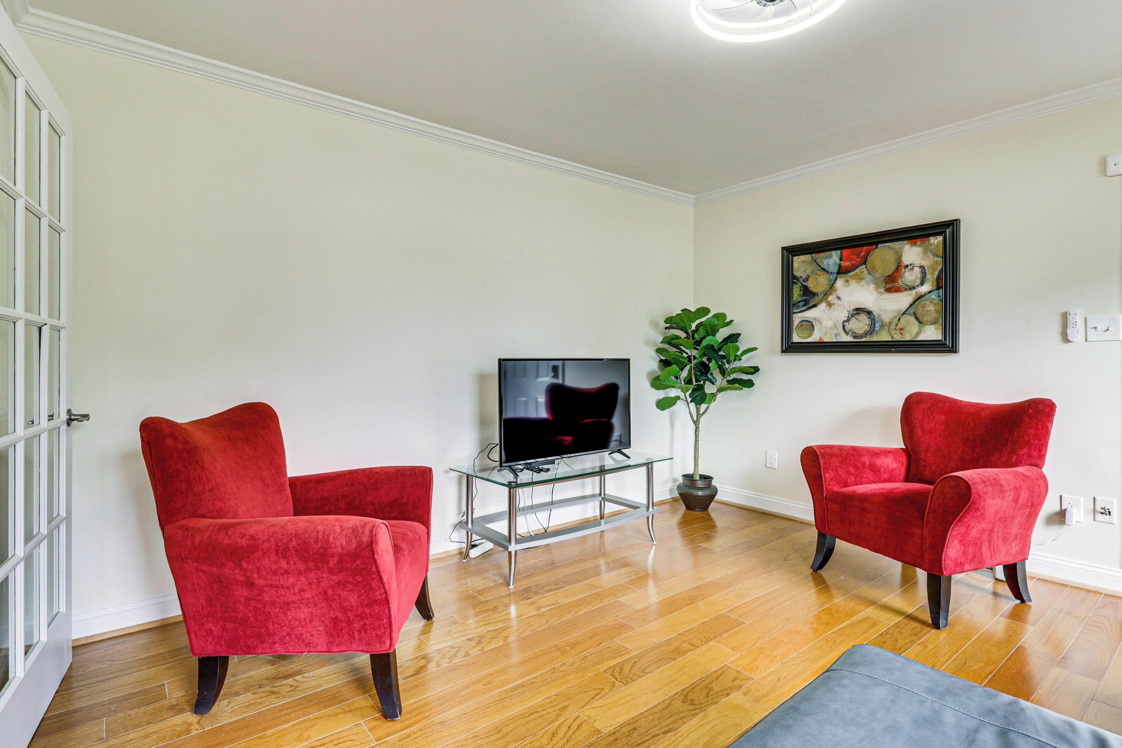 A living room with two red armchairs, a glass coffee table, a television, and a potted plant.