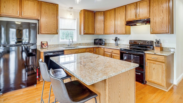 A modern kitchen with wooden cabinets, granite countertops, stainless steel appliances, and a bar area with stools. - Walk to Dtwn & Campus! Spacious Hampton Home (Hampton)