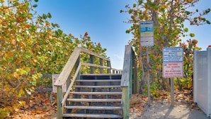 A wooden staircase leading to a beach area with signs indicating dog-friendly access and rules about unattended items. - Dogs Welcome, Steps to Ocean: Cocoa Beach Getaway (Cocoa Beach)