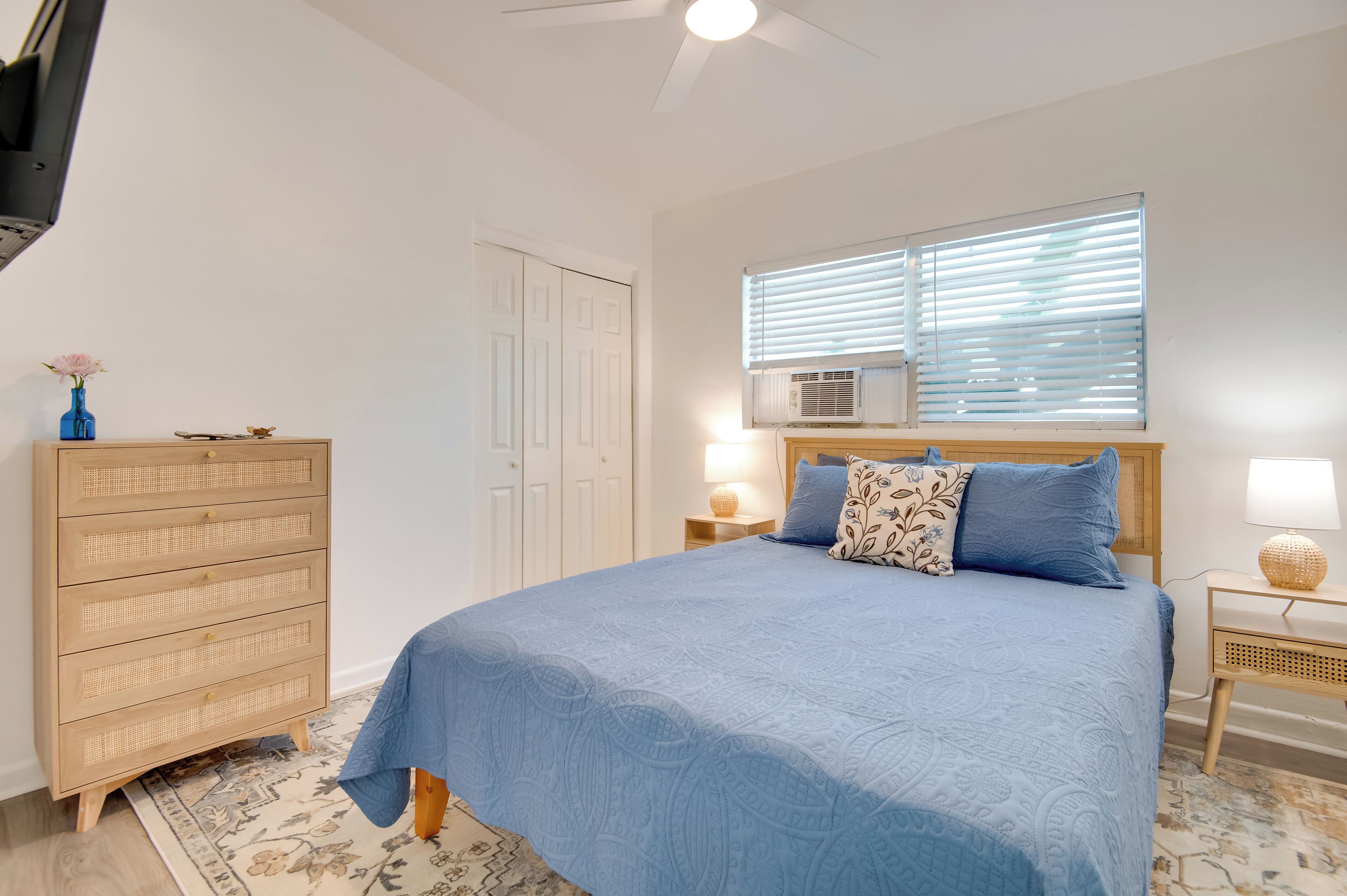 Un dormitorio con cama, cómoda, mesita de noche, lámpara y ventana con persianas.