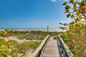 A wooden boardwalk leading to a beach with sand dunes and sparse vegetation. - Dogs Welcome, Steps to Ocean: Cocoa Beach Getaway (Cocoa Beach)