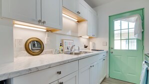 A kitchen with white cabinets, a green door, a marble countertop, a sink, and a framed picture. - Dogs Welcome, Steps to Ocean: Cocoa Beach Getaway (Cocoa Beach)