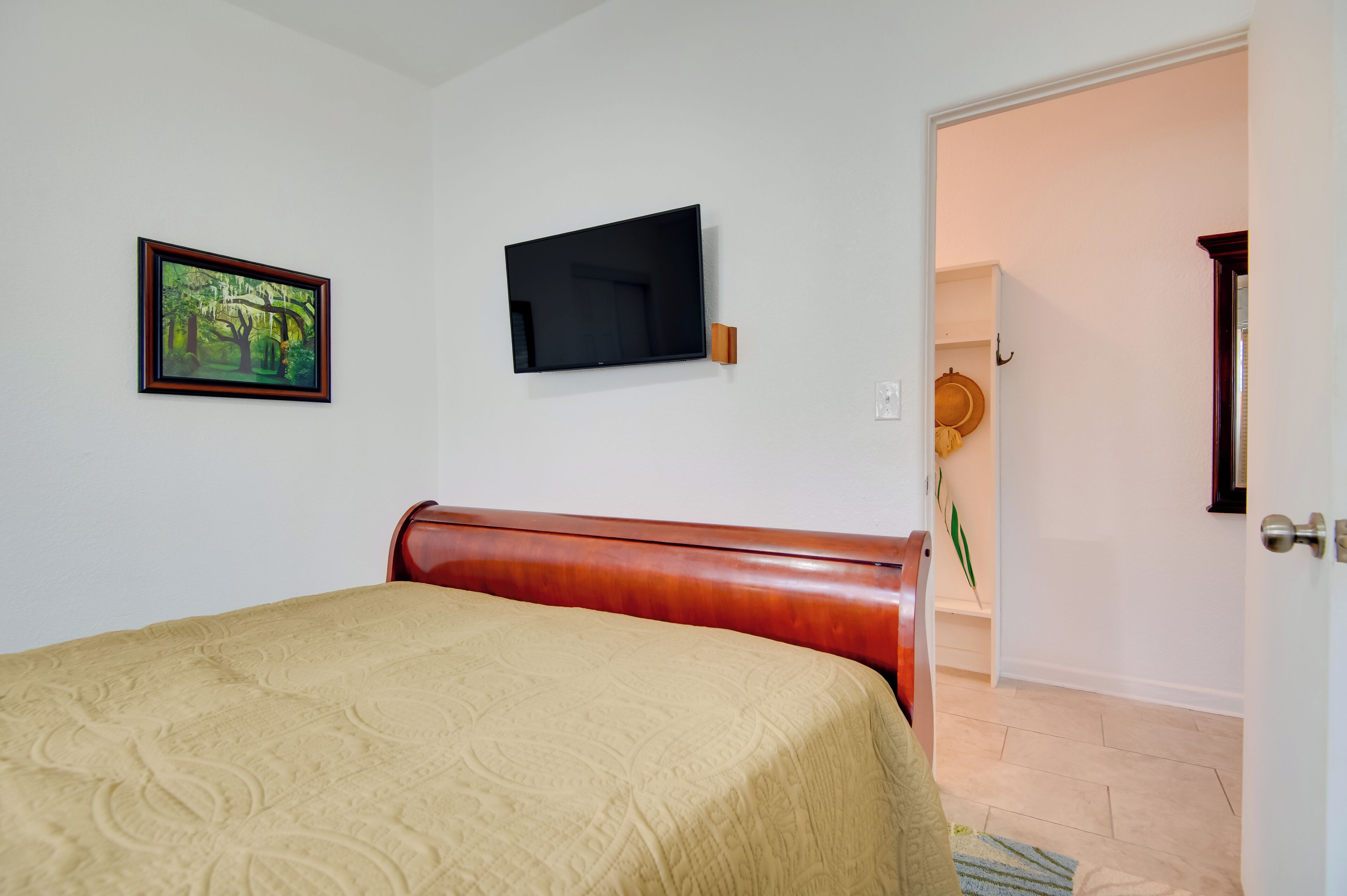 Une chambre à coucher avec un lit, un téléviseur fixé au mur et une porte donnant sur une autre pièce.
