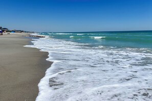 Ein Strand mit wellen, die an das Ufer schlagen, einem klaren Himmel und Gebäuden im Hintergrund.