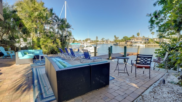 Une terrasse extérieure aménagée avec un canapé, des fauteuils et une table, offrant une vue sur une marina avec des bateaux et un ciel dégagé.