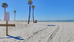 Une plage de sable avec des palmiers et un panneau indiquant les règles à respecter sur la plage.