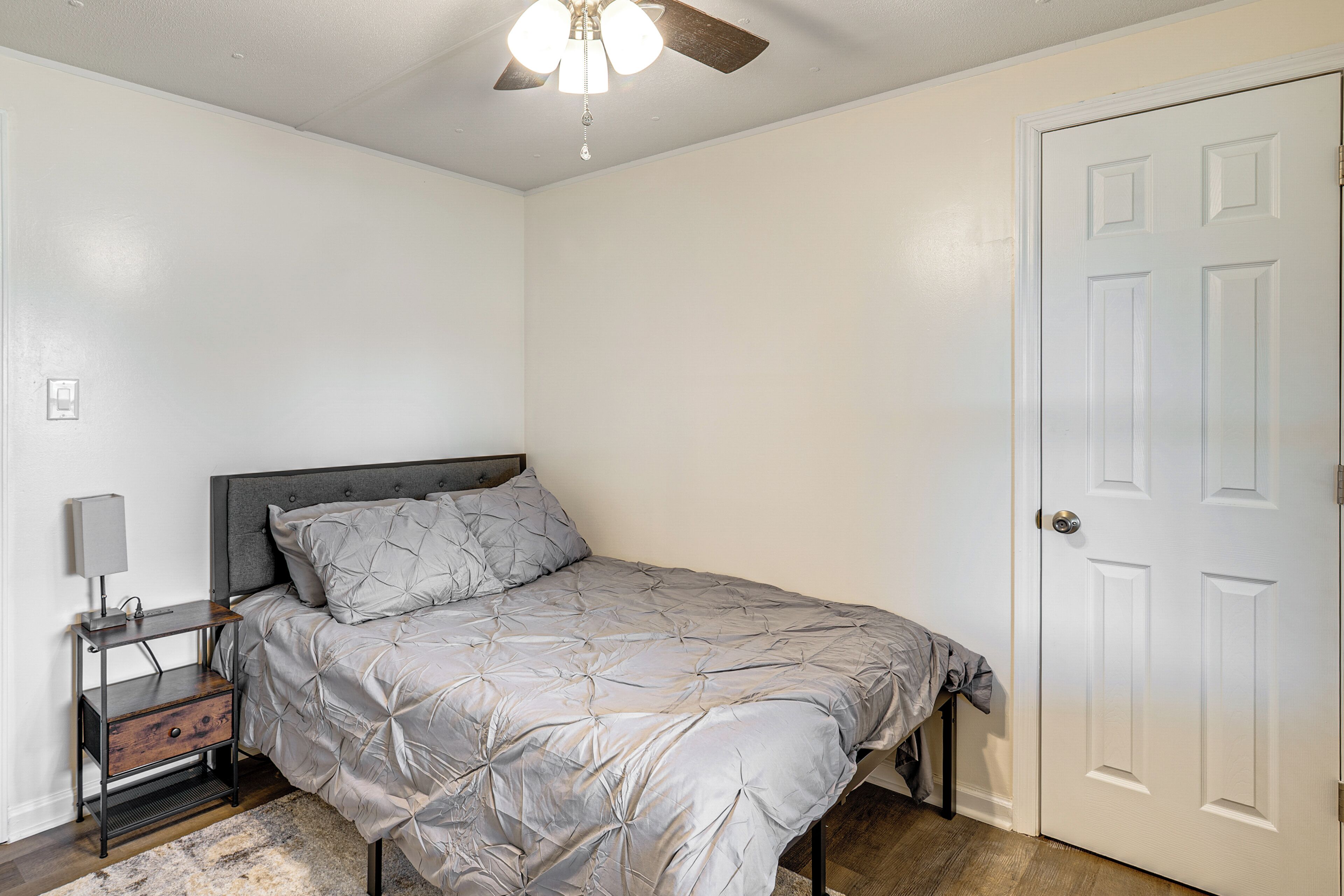 A bedroom with a bed, a nightstand, a ceiling fan, and a white door.