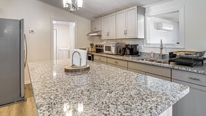 Una cocina con encimeras de granito, armarios blancos, refrigerador de acero inoxidable, cafetera y microondas.