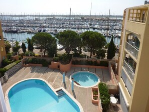 Blick auf eine Marina mit zahlreichen Booten, ein Poolbereich mit zwei Pools und ein Gebäude mit Balkonen mit Blick auf die Marina.