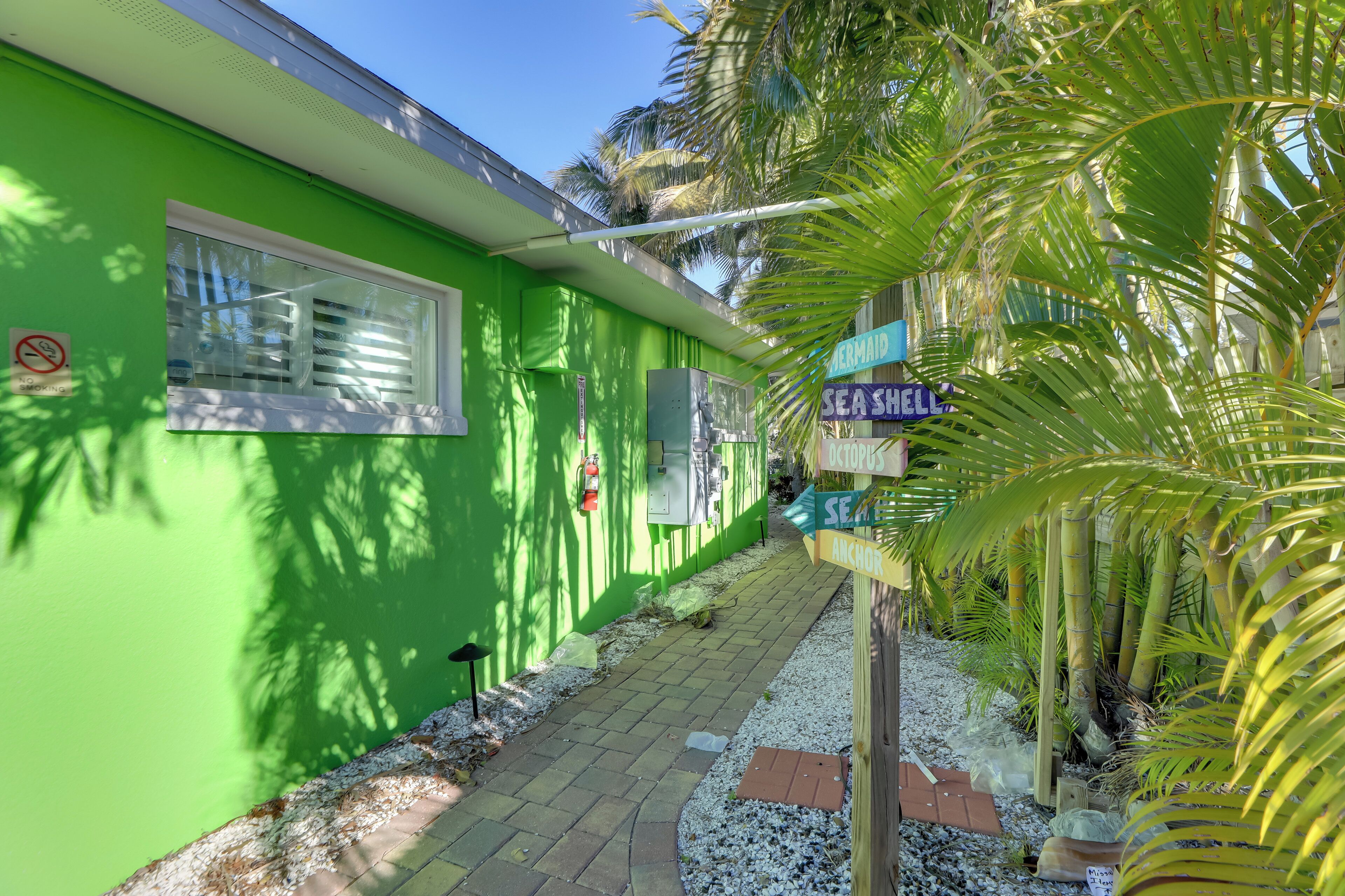 A green building with a window, a sign for 'SEASHELL', and palm trees.