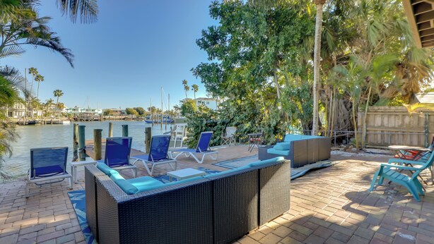 A patio area with outdoor furniture, a view of the water, and palm trees. - Walk to Everything! Johns Pass Gem w/ Dock Access (Madeira Beach)