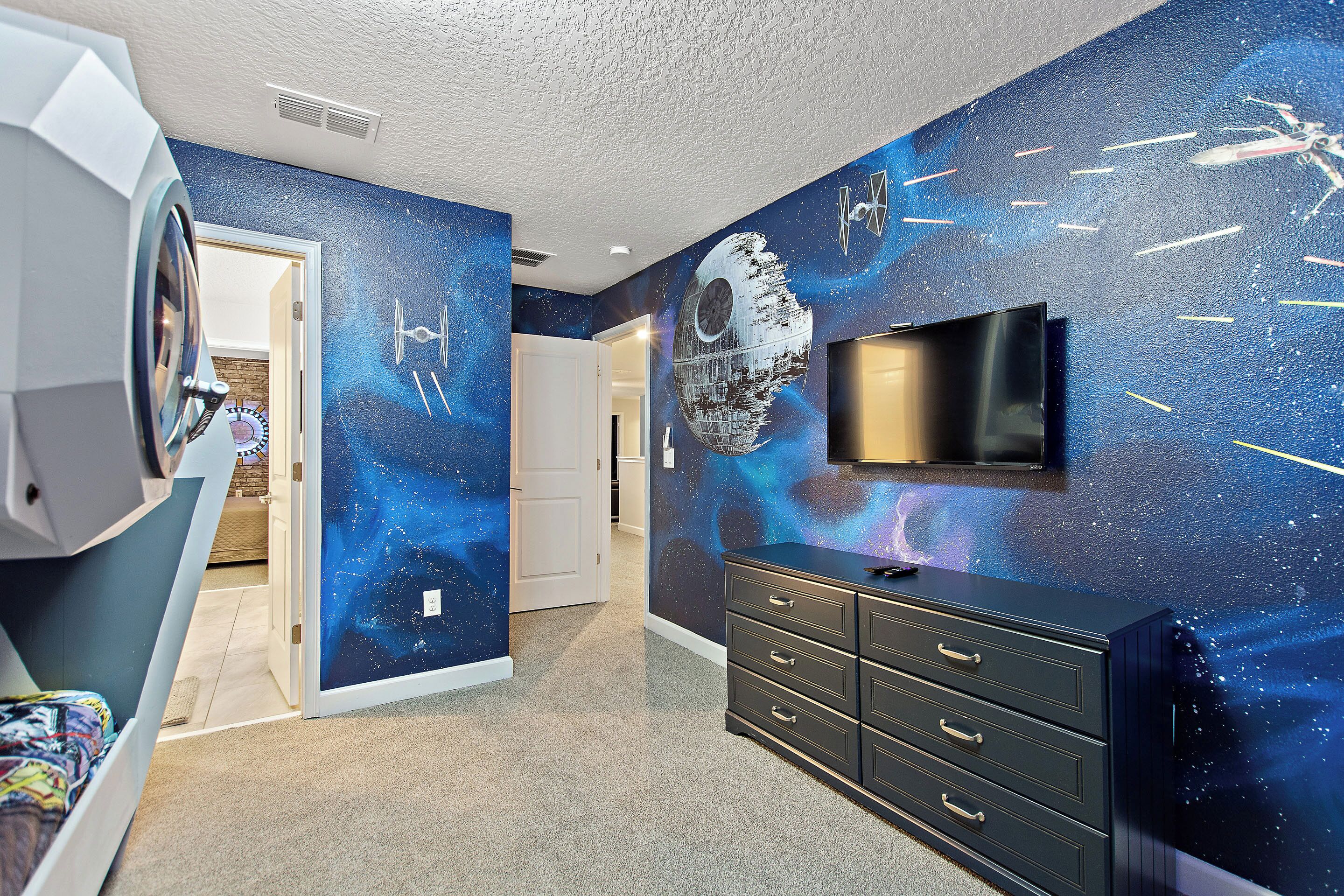 A bedroom with a Star Wars themed wall mural, a bed, a dresser, and a television.